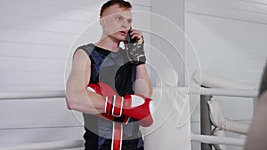 Serious man fighter is talking on smartphone during break of training on ringside.