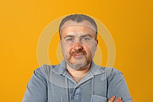 Serious man with folded arms and a deadpan expression posing in front of a yellow background photo
