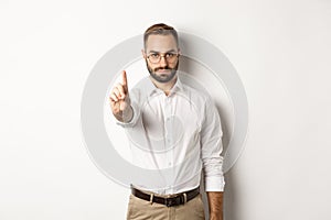 Serious man in glasses showing stop sign, shaking finger to prohibit and forbid, standing over white background