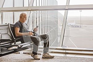 A serious man with headphones looks at his smartphone, sitting at the airport