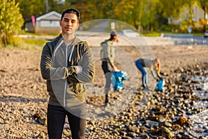 Serious man with his armes crossed at beach with group of volunteers on sunny day