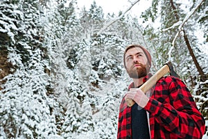 Serious man holding axe and walking in winter forest