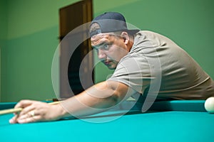 A serious man holding a cue in his hands aims at a billiard ball. A man plays Russian billiards with his friends while
