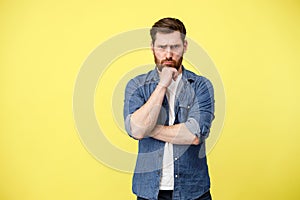 Serious man houghtfully hold hand near beard in yellow background