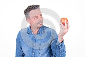 Serious man looks longingly at a red apple in his hand  isolated over white background photo