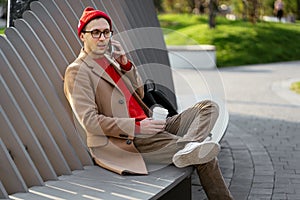 Serious man on phone call sit with coffee on park bench. Freelance casual businessman use smartphone