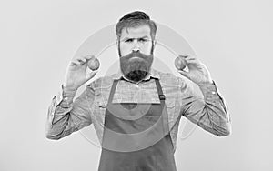 Serious man in red apron holding fresh limes citrus fruits yellow background, fruiterer photo