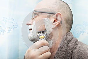 Serious man shaving his beard by razor blade