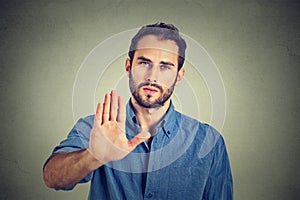 Serious man showing stop gesture isolated on gray wall background