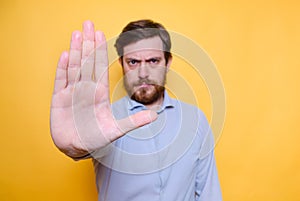 Serious man shows a forbidding gesture on a yellow background