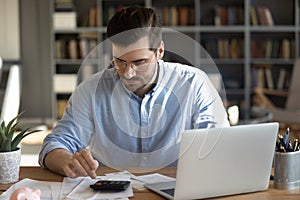 Serious man sit at desk use calculator calculates monthly expenses