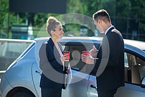 Serious man and smiling woman with glasses of coffee near car