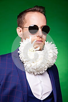 Serious man in suit and with flowers in beard looking at camera