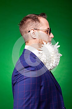 Serious man in suit and with flowers in beard looking at camera