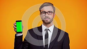 Serious man in suit holding green screen smartphone, online schedule app