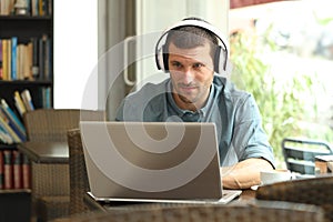 Serious man using a laptop with headphones in a bar