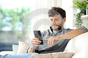 Serious man using phone on a couch at home
