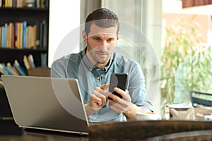 Serious man using smart phone and laptop in a bar