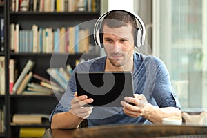 Serious man using tablet and headphones in a coffee shop