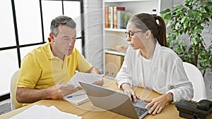 Serious man and woman business workers working together, reading a document online on their laptop at the office - professional