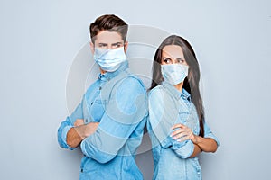 Serious man and woman with crossed hands standing back to back after quarrel wear medical safety sterile mask on face