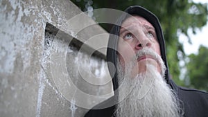 Serious mature bald bearded man with hoodie thinking against concrete wall outdoors