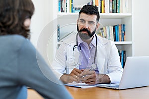 Serious mature doctor with hipster beard listening to patient