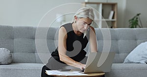 Serious mature homeowner woman using financial application on laptop