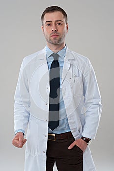 Serious mature male doctor standing on grey background