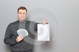 Serious mature man is holding US dollars and white blank paper sheet