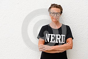 Serious mature nerd woman with arms crossed wearing big eyeglasses and standing against white background outdoors