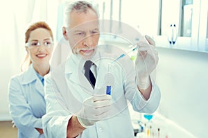 Serious mature scientist pouring liquid into test tube