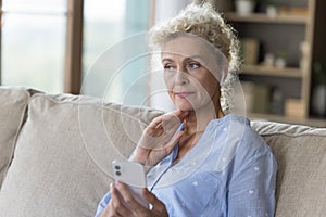 Serious mature senior woman lady holding mobile phone on couch