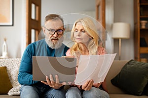 Serious Mature Spouses With Laptop Doing Paperwork Together At Home