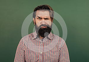 serious mature teacher on background of blackboard. brutal bearded man wear casual checkered shirt and frowns. express