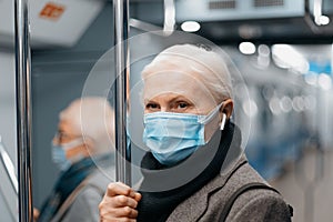 serious mature woman in a protective mask standing in a subway car .