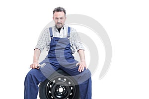 Serious mechanic with spanner sitting on car tire