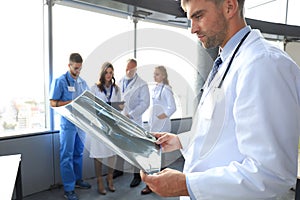 Serious medical doctor looking closely at the x-ray, collegues at the background