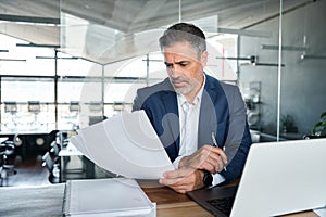 Serious mid aged business man ceo checking corporate financial document.