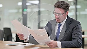Serious Middle Aged Businessman doing Paperwork in Office