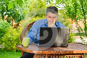 Businessman drinking coffee and reading news using laptop in his garden