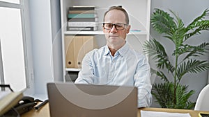 Serious middle-aged man doubting ideas while concentrating on his laptop work in a professional office space