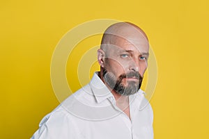 Serious middle-aged man with folded arms and a deadpan expression posing in front of a yellow background with copy space