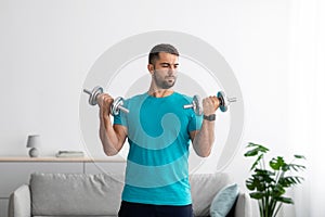 Serious millennial european male athlete in blue t-shirt do strength exercises for arms and lifting dumbbells