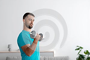 Serious millennial muscular european guy doing arm exercises, lifts dumbbell in living room interior