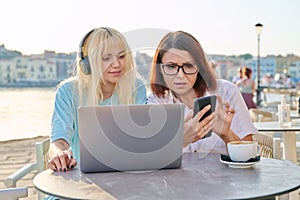 Serious mother and teenage daughter together in outdoor cafe looking at laptop