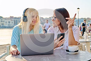 Serious mother and teenage daughter together in outdoor cafe looking at laptop