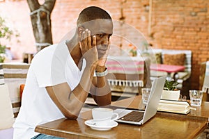 Serious multiracial businessman using laptop in cafe with head in hands in cafe. Video call and read finance information