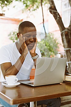 Serious multiracial businessman using laptop in cafe with head in hands in cafe. Video call and read finance information