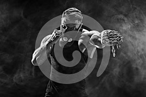 Serious muscular fighter doing the punch with the chains braided over his fist.